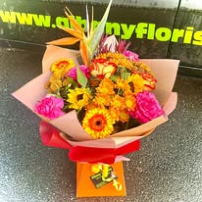 Tropical Sunset - Bursting with warm shades of gold, orange, red, and vibrant pink, this eye-catching hand-tied bouquet captures the beauty and energy of a glowing sunset. Rich in colour, texture, and seasonal charm, it is thoughtfully arranged to create a cheerful and uplifting display. Perfect for birthdays, congratulations, thank-you gifts, celebrations, or simply brightening someone's day, this bouquet brings warmth, happiness, and a touch of sunshine wherever it goes.