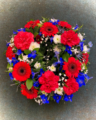 Wreath - A striking funeral wreath designed in bold red, white, and blue tones, symbolising honour, respect, and everlasting remembrance. Thoughtfully arranged in a traditional circular design, this tribute represents the enduring nature of love and memory. Its vibrant colours and elegant presentation create a heartfelt expression of sympathy, making it a meaningful way to celebrate a life of courage, devotion, and cherished memories while offering comfort to family and friends.