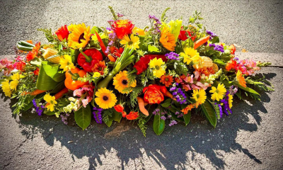 Harvest Memories Casket Spray - A unique and deeply personal funeral tribute inspired by a love of the countryside, gardening, and the harvest season. Designed with vibrant golden, orange, red, and purple tones alongside carefully chosen natural elements, this casket spray celebrates a life rich in character, passion, and cherished memories. Its abundant, rustic style creates a heartfelt farewell, offering comfort to family and friends while honouring the individuality and legacy of a loved one in a truly meaningful way.